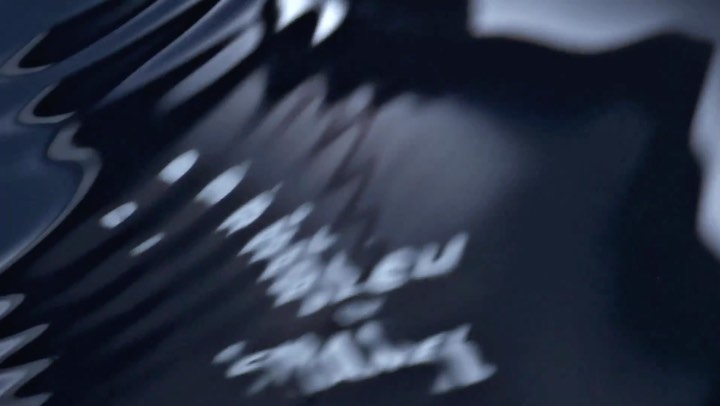 Abstract image of dark, rippling liquid surface with light reflections and blurred text, creating a mysterious and intriguing visual texture.