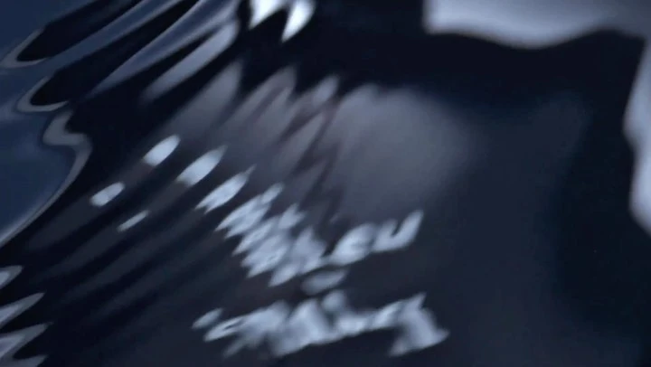 Abstract image of dark, rippling liquid surface with light reflections and blurred text, creating a mysterious and intriguing visual texture.