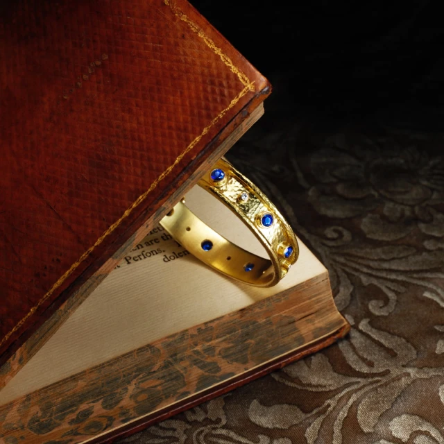 Close-up of a vintage book with a gold and blue jeweled bracelet resting on its pages against a dark, textured backdrop.
