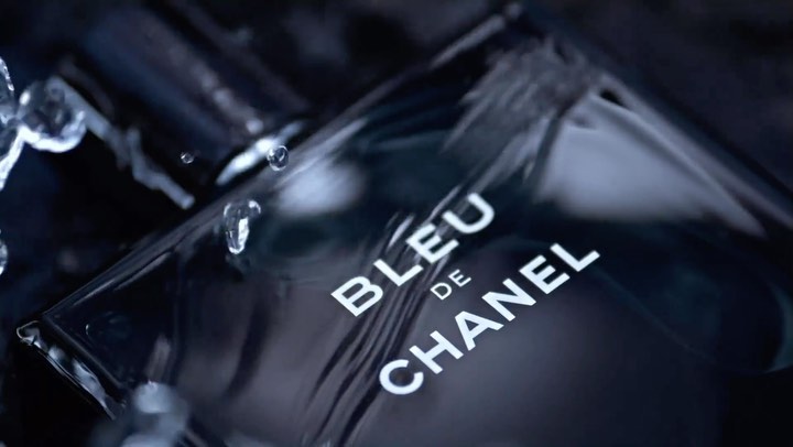 Close-up of a dark, glossy bottle of Bleu de Chanel cologne, surrounded by water droplets, creating a luxurious and refreshing impression.