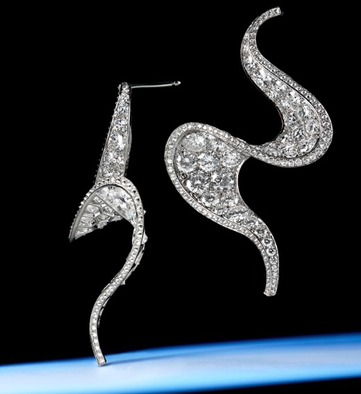 Two elegant silver and diamond swirl earrings set against a gradient blue and black background, suggesting high-end jewellery fashion.