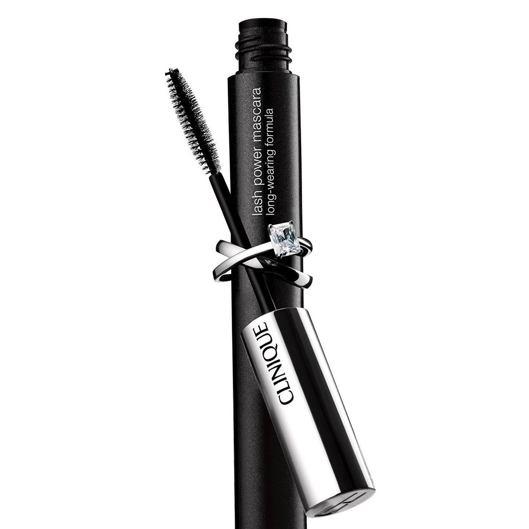 Clinique lash power mascara in black with brush applicator, adorned with a diamond ring on a white backdrop, beauty product.