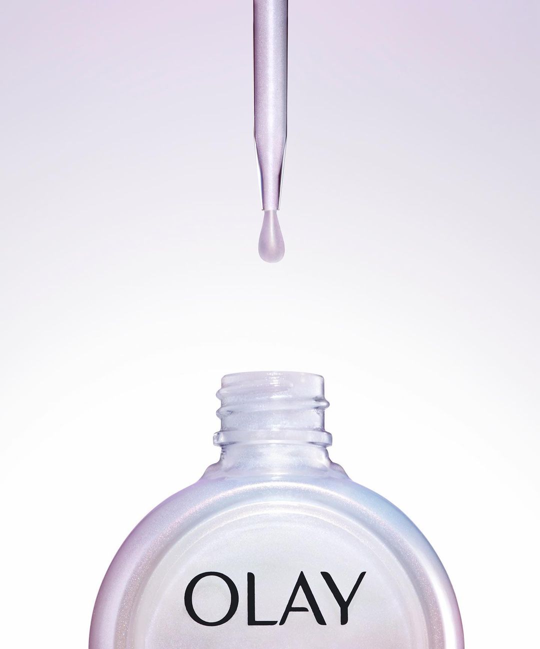 Close-up of a dropper dispensing liquid into a bottle of Olay skincare serum, set against a gradient white and purple background.