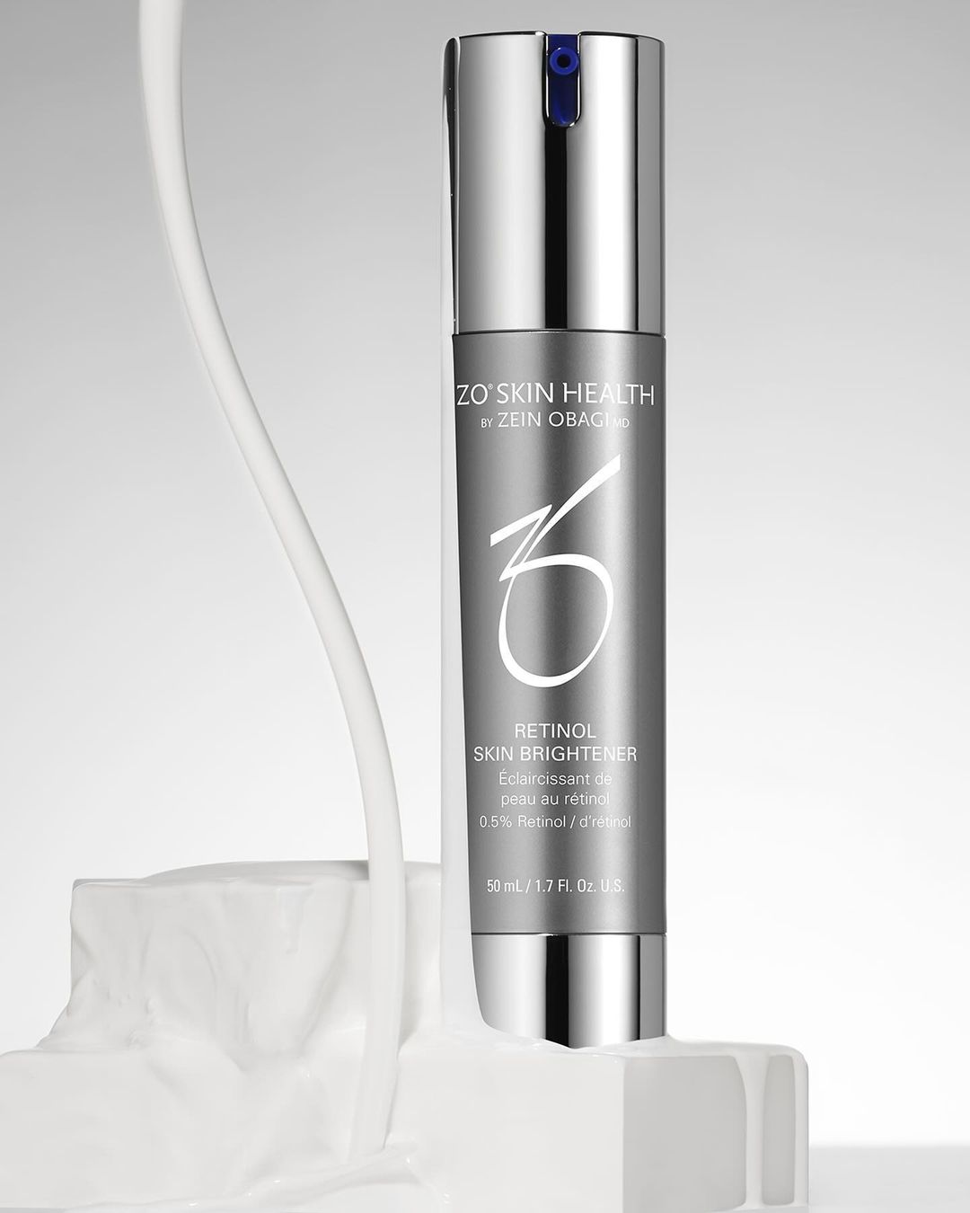 Silver ZO Skin Health Retinol Skin Brightener bottle on white textured block against light grey background. Product shot for beauty industry.