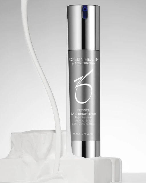Silver ZO Skin Health Retinol Skin Brightener bottle on white textured block against light grey background. Product shot for beauty industry.