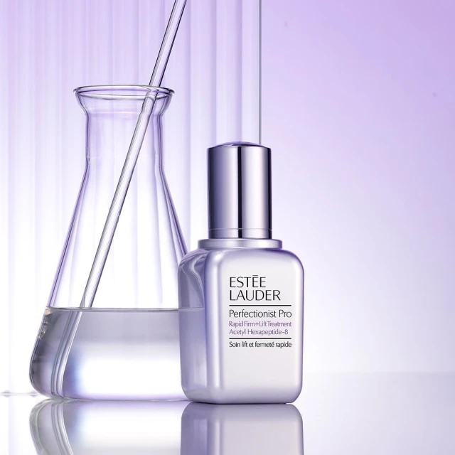 Estée Lauder Perfectionist Pro skincare product shot in a lab-like setting with a beaker and clear liquid against a gradient purple background.