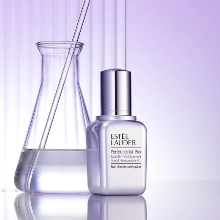 Estée Lauder Perfectionist Pro skincare product shot in a lab-like setting with a beaker and clear liquid against a gradient purple background.