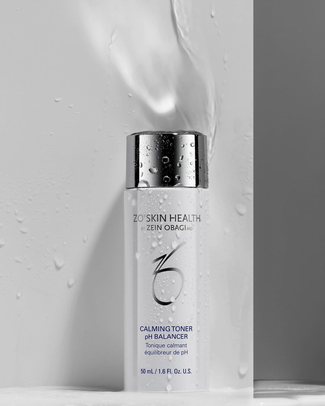 Product shot of ZO Skin Health Calming Toner, featuring a sleek white bottle with a silver cap, accented by water droplets and a clean background.
