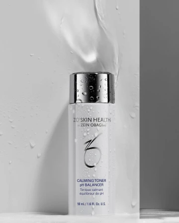 Product shot of ZO Skin Health Calming Toner, featuring a sleek white bottle with a silver cap, accented by water droplets and a clean background.