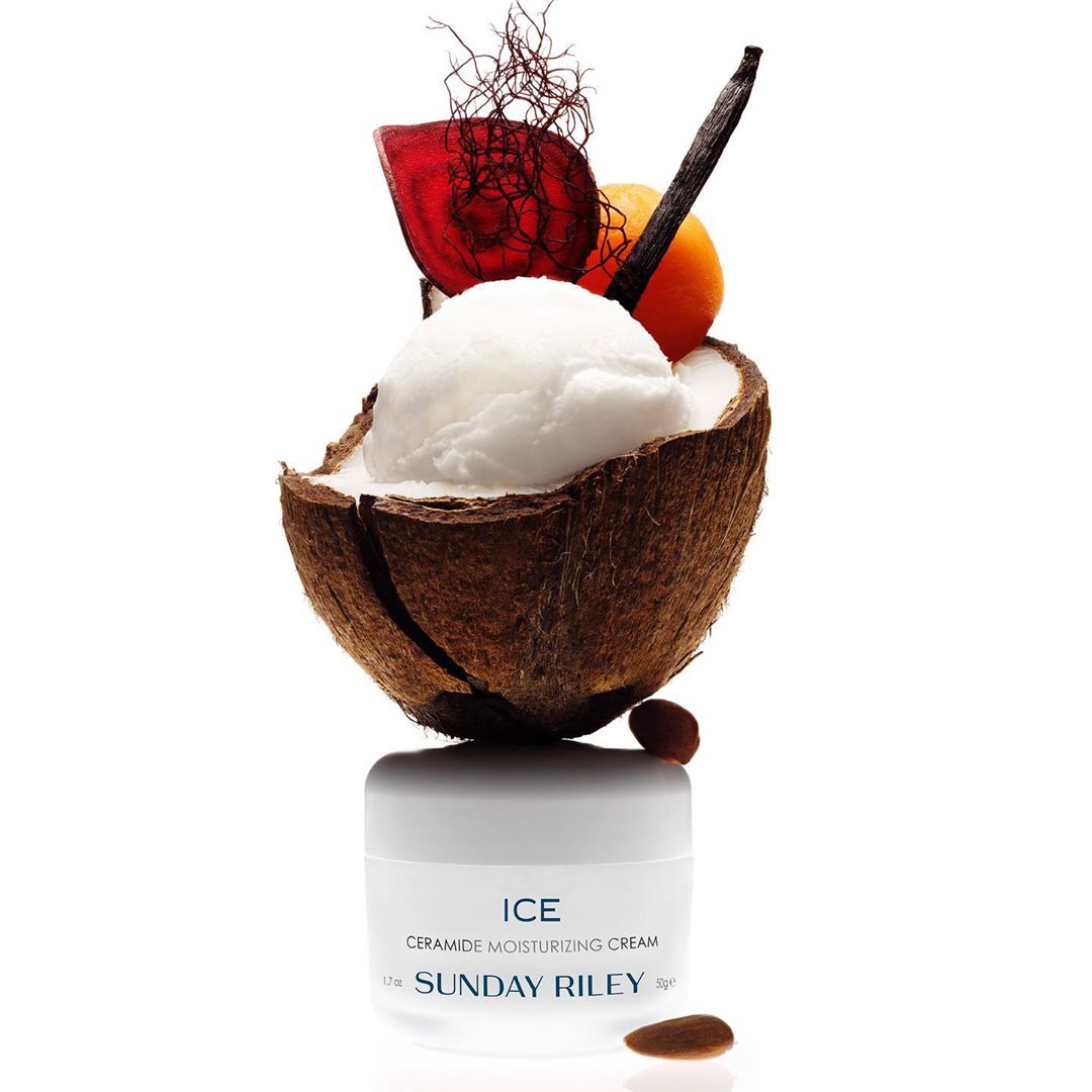 Close-up studio shot of a jar of white facial cream topped with coconut shell filled with white cream, fruit and vegetable garnishes.