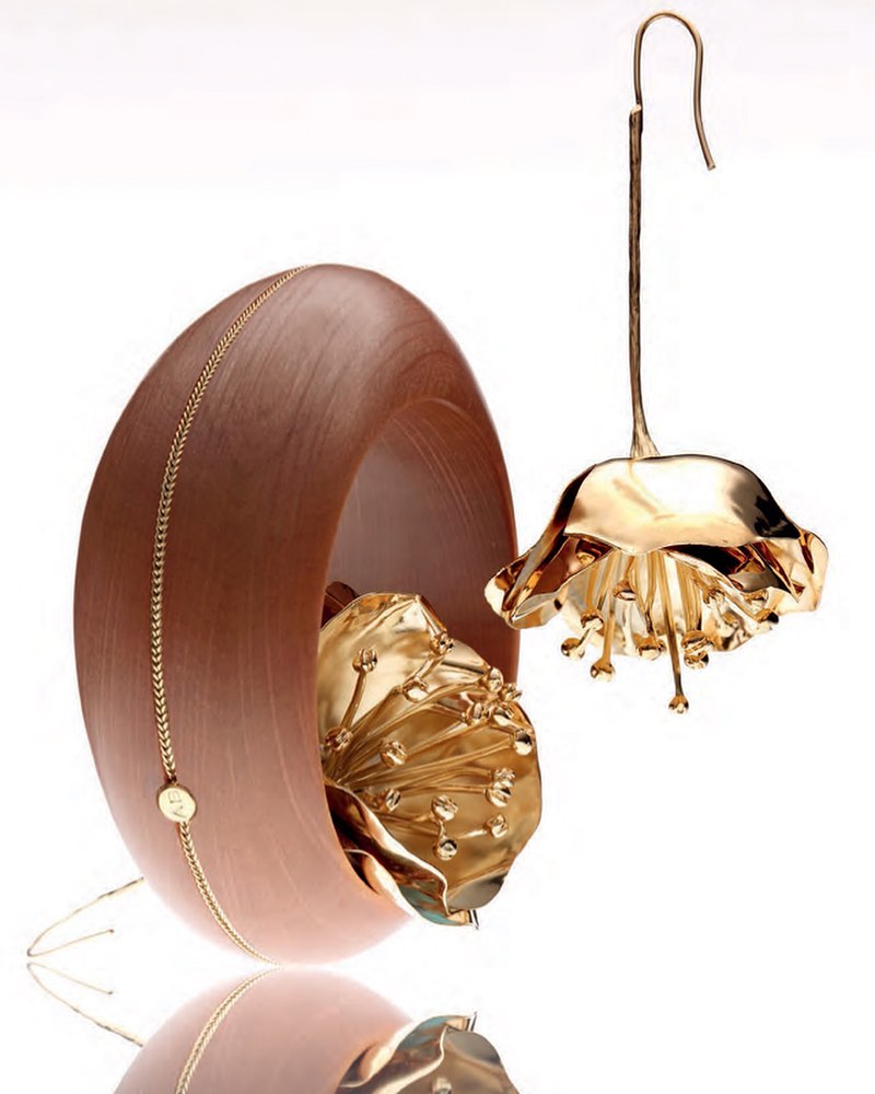 Elegant product shot of golden flower-shaped earrings beside a wooden bowl against a white background, capturing a blend of sophistication and natural beauty.