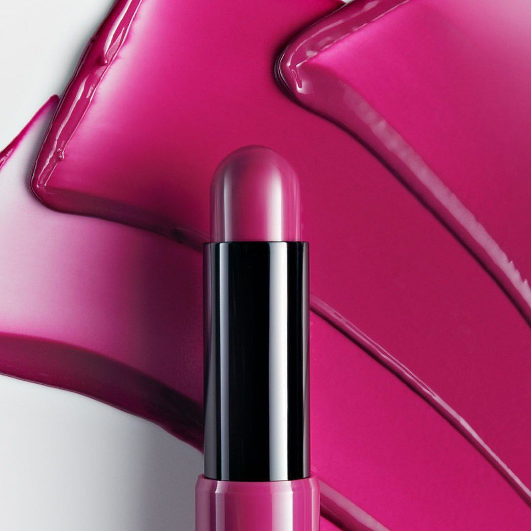 Close-up studio shot of pink lipstick with black packaging, against background of smeared pink cosmetic product.