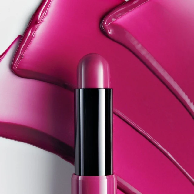 Close-up studio shot of pink lipstick with black packaging, against background of smeared pink cosmetic product.