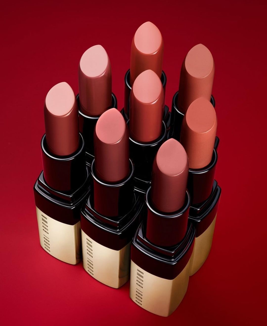 Close-up shot of a set of lipsticks in varying shades of nude and red, displayed against a deep red background.