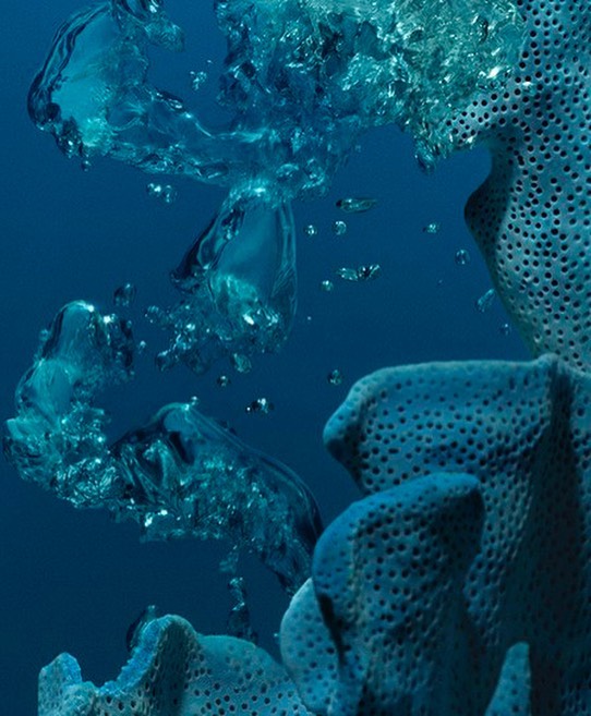Underwater view of turquoise water with rising translucent bubbles and coral, creating a serene and abstract natural scene.