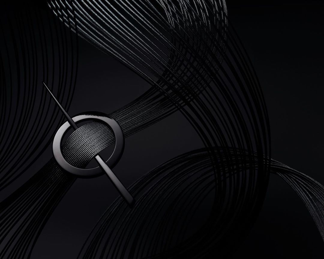 Abstract, high-angle studio shot: Black metal pin intersecting a circular ring resting on a surface with curved black strings.
