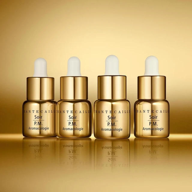 Four gold Chantecaille Soir P.M. Aromacologie bottles with droppers are displayed against a shiny gold background for Beauty advertising.