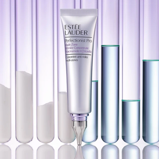Silver tube of Estee Lauder Perfectionist Pro wrinkle concentrate against a background of glass test tubes with clear and white liquid.