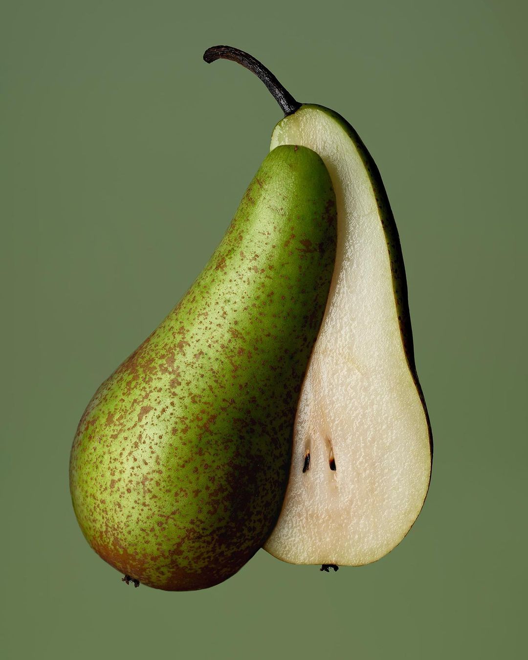Close-up of a whole green pear and a pear cut in half, showcasing the seeds and flesh, against a solid light green background.
