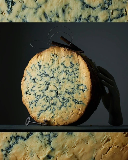 Close-up of a cut wheel of bleu cheese with mold patterns, a metal key, and a decorative metal hairpin against a dark background.