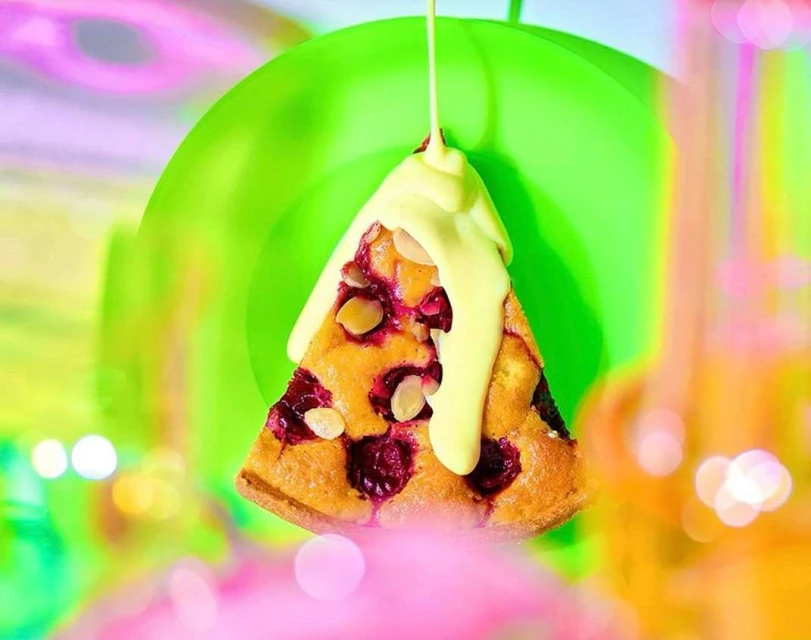 Overhead view of a slice of cherry pie with drizzled sauce, showcasing a colorful background of green, pink, and orange bokeh.