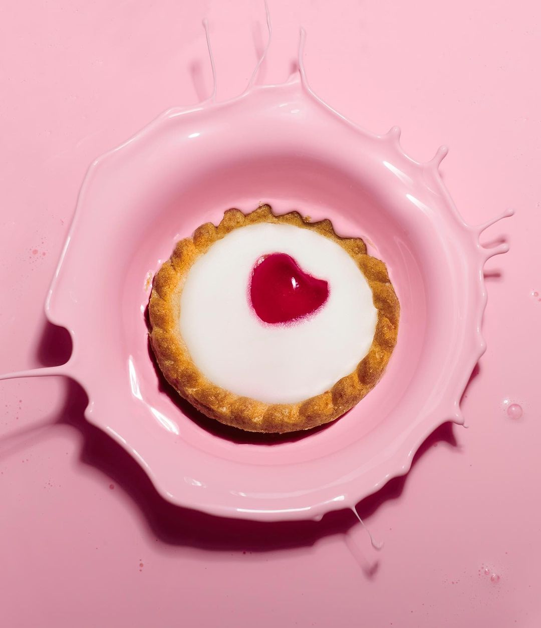 Close-up of a heart-topped tart splashing in pink liquid. The tart is centered, surrounded by a pink milky liquid with splashing.