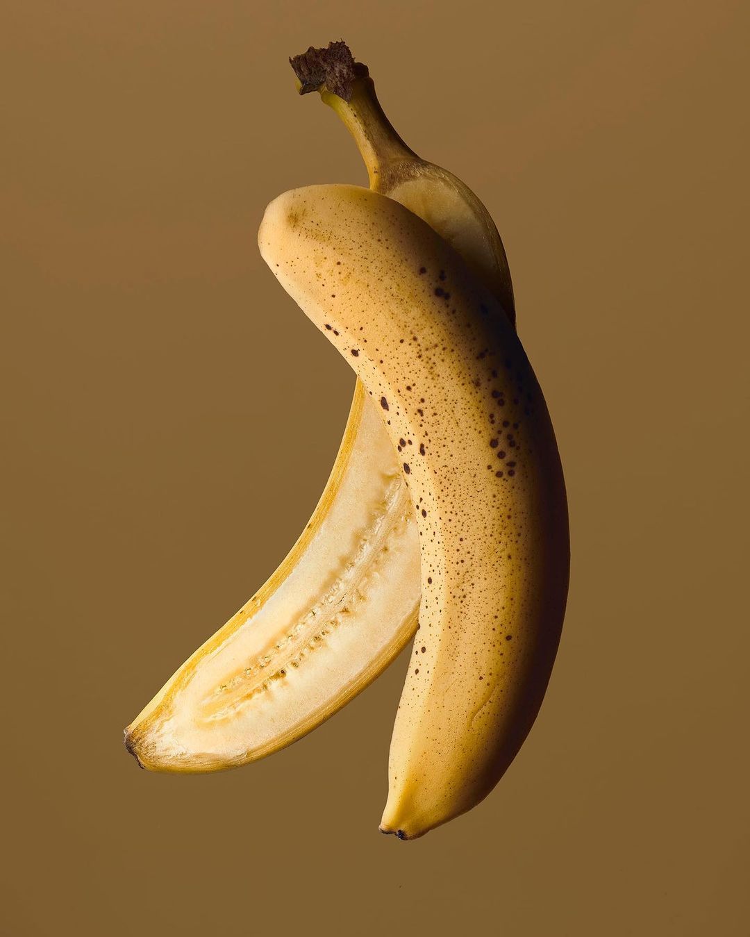 Ripe banana with its peel partially removed on a tan background, highlighting texture and color variations of the fruit.