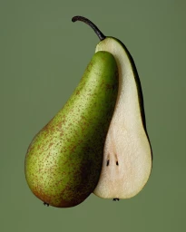 Close-up studio photograph of a whole green pear next to a sliced half showing seeds against a solid sage green backdrop
