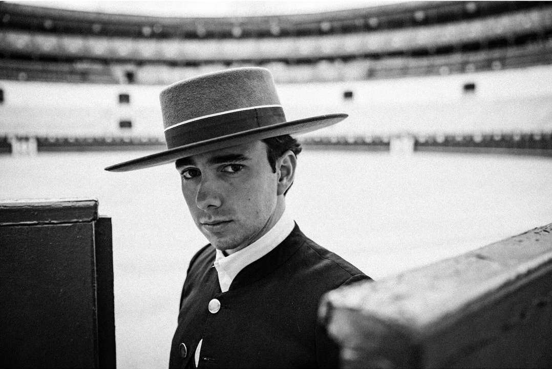 Portrait of bullfighter wearing hat and suit in arena setting. Black and white photography with shallow depth of field, eye-level view.