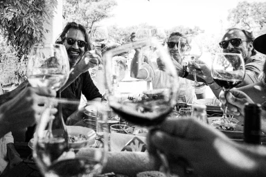 Black and white photograph of a group of adults raising wine glasses for a toast around an outdoor table.