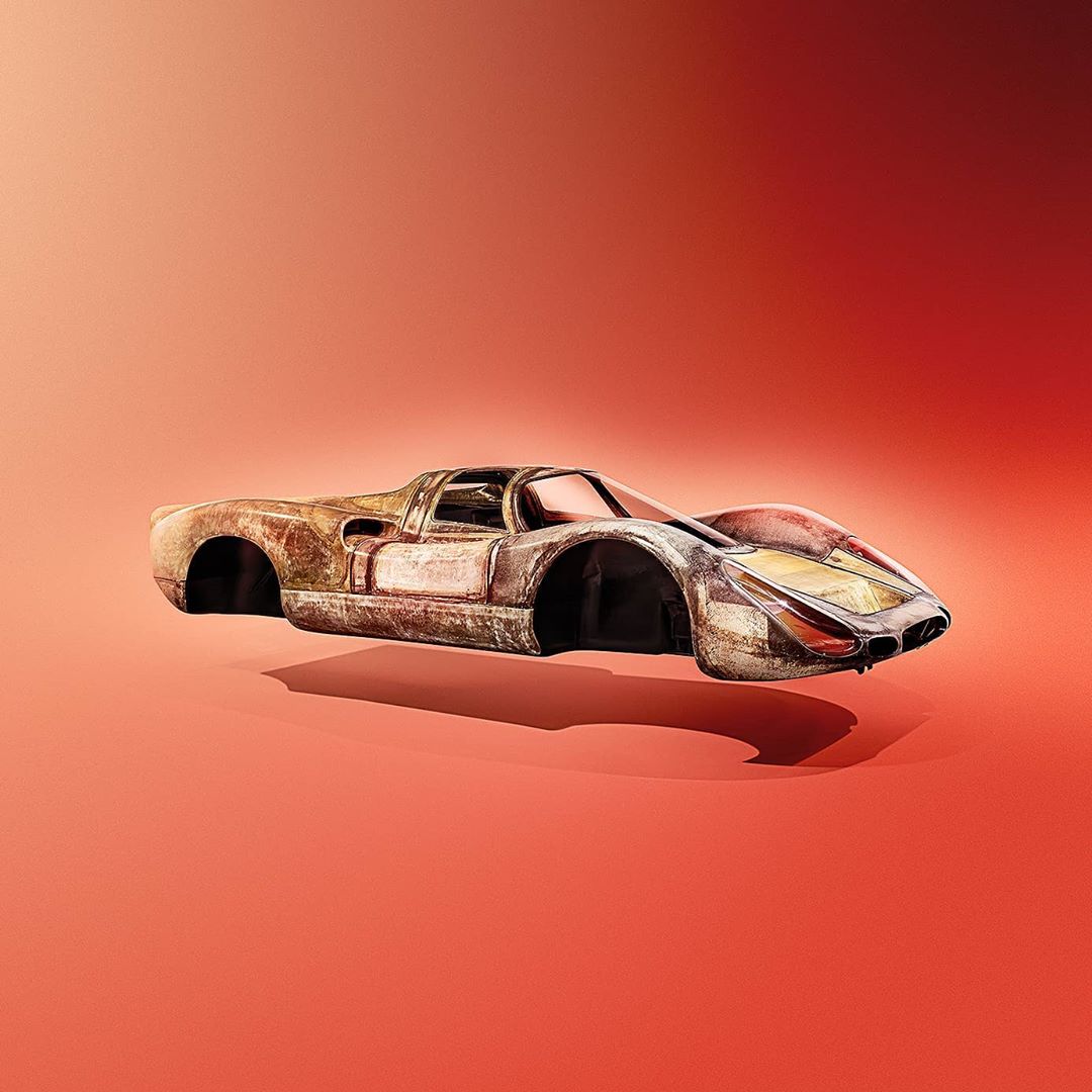 Vintage, weathered race car body with no wheels is set against an orange background in a studio shot, showcasing texture and design.