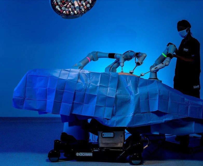 Robot-assisted surgery with robotic arms and surgeon in sterile medical environment, surgical bed, and operating room lighting.