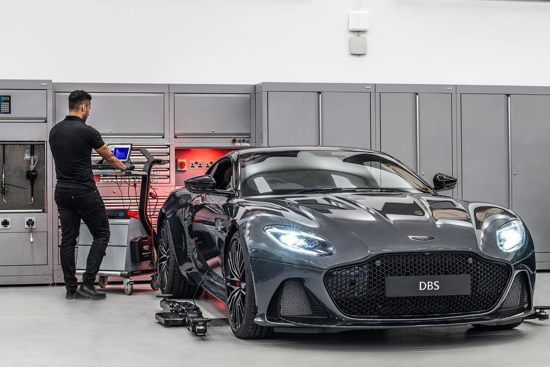 Gray Aston Martin DBS Superleggera parked in an auto service garage with a mechanic using computer equipment to diagnose the car.