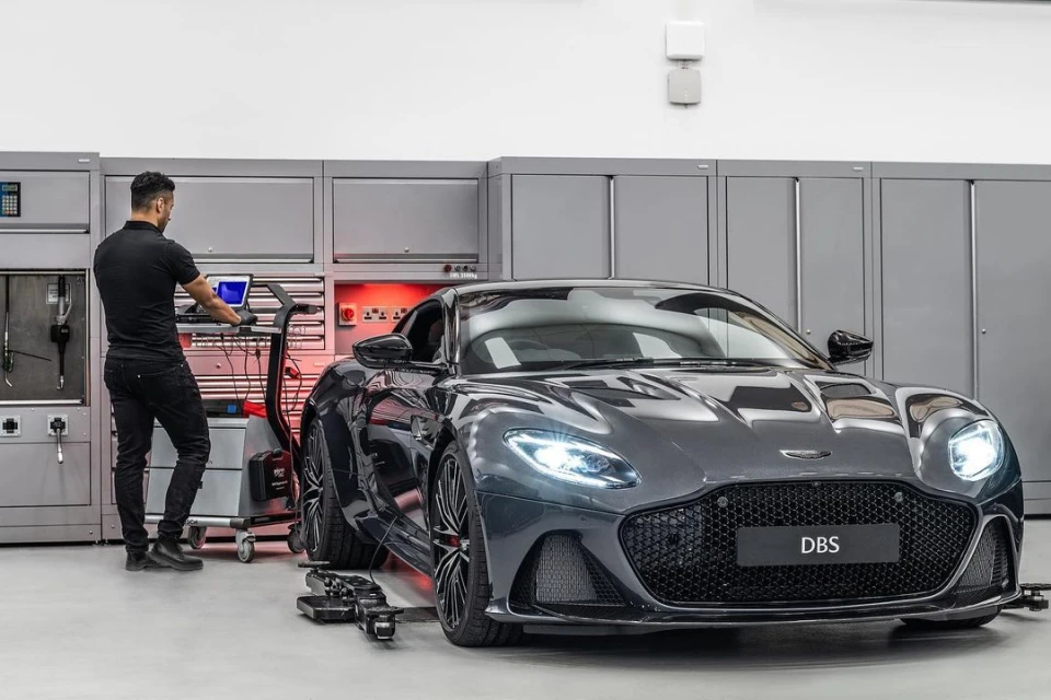 Gray Aston Martin DBS Superleggera parked in an auto service garage with a mechanic using computer equipment to diagnose the car.