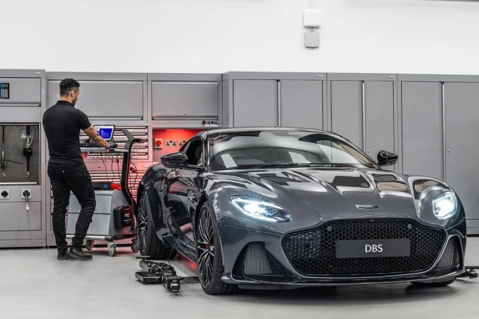 Gray Aston Martin DBS Superleggera parked in an auto service garage with a mechanic using computer equipment to diagnose the car.