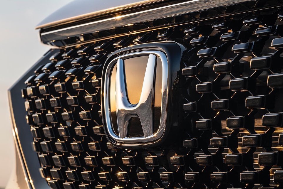 Close-up of the front grille and logo of a black car. Car grille has a repeating geometric pattern. Silver 'H' logo in the center.
