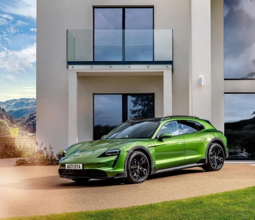 Green Porsche Taycan Cross Turismo parked in front of a modern house on a sunny day, showcasing automotive design and luxury lifestyle.