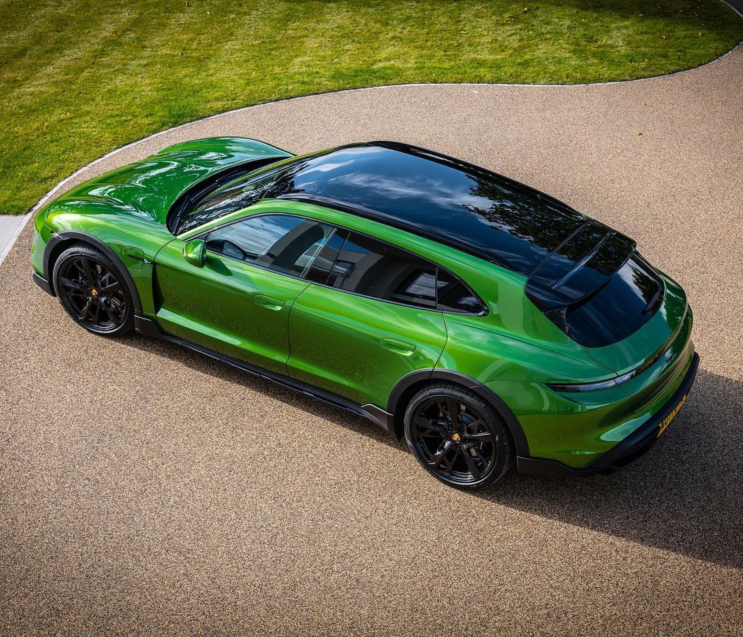 Overhead shot of a green Porsche Taycan Cross Turismo parked on a gravel driveway with a green lawn in the background.