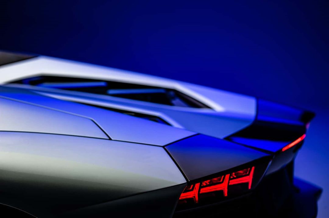 Close-up of the rear of a silver Lamborghini, highlighting its taillights and angular design against a deep blue background.