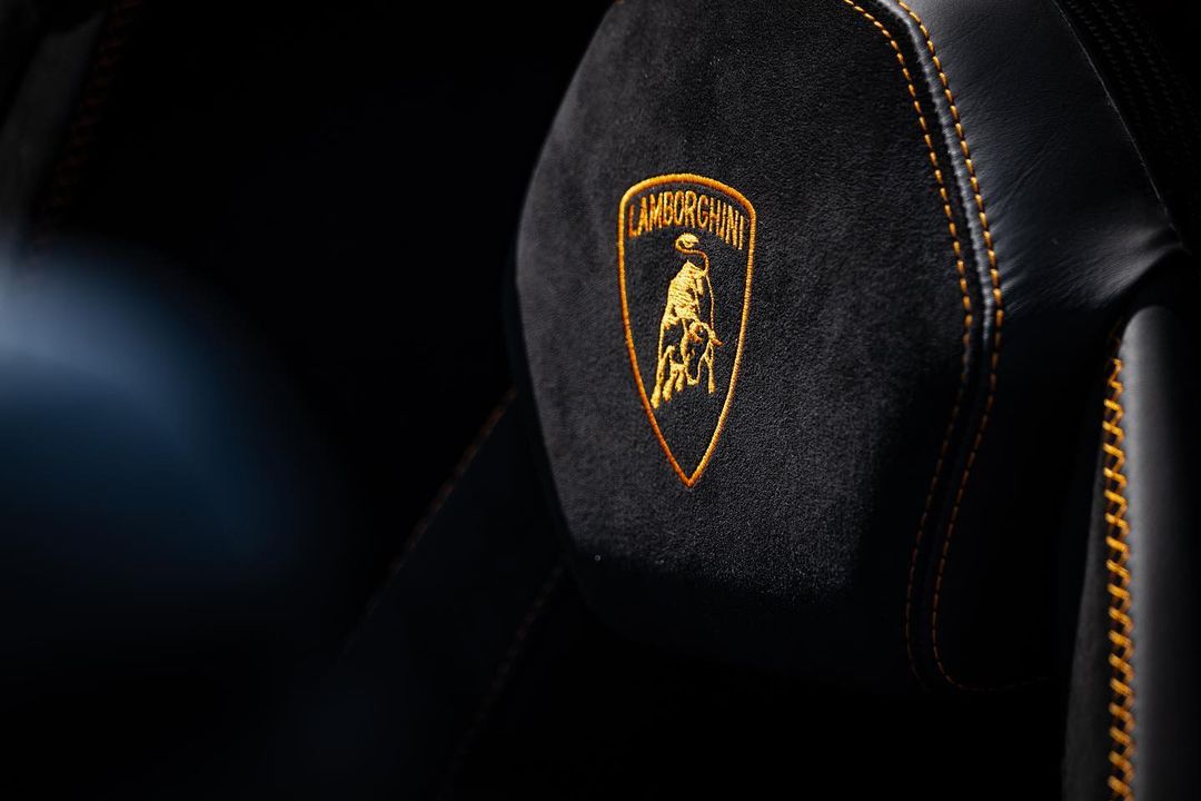 Close-up of a black car seat headrest with a gold Lamborghini logo, highlighting automotive luxury and Italian design.