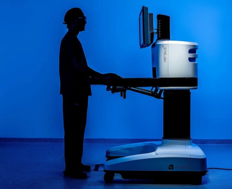 A surgical robot is used by a doctor silhouette, standing on a tiled floor in front of a gradient blue background in an indoor environment.