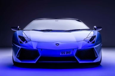Front view of a blue luxury sports car with a custom license plate parked against a gradient background.