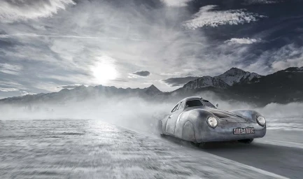 Vintage silver car driving through a misty snowy landscape with distant mountains under a dramatic cloudy sky