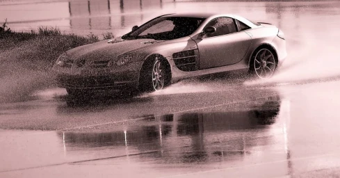 Silver sports car driving through water splashes on a wet track, captured by Richard Seymour.