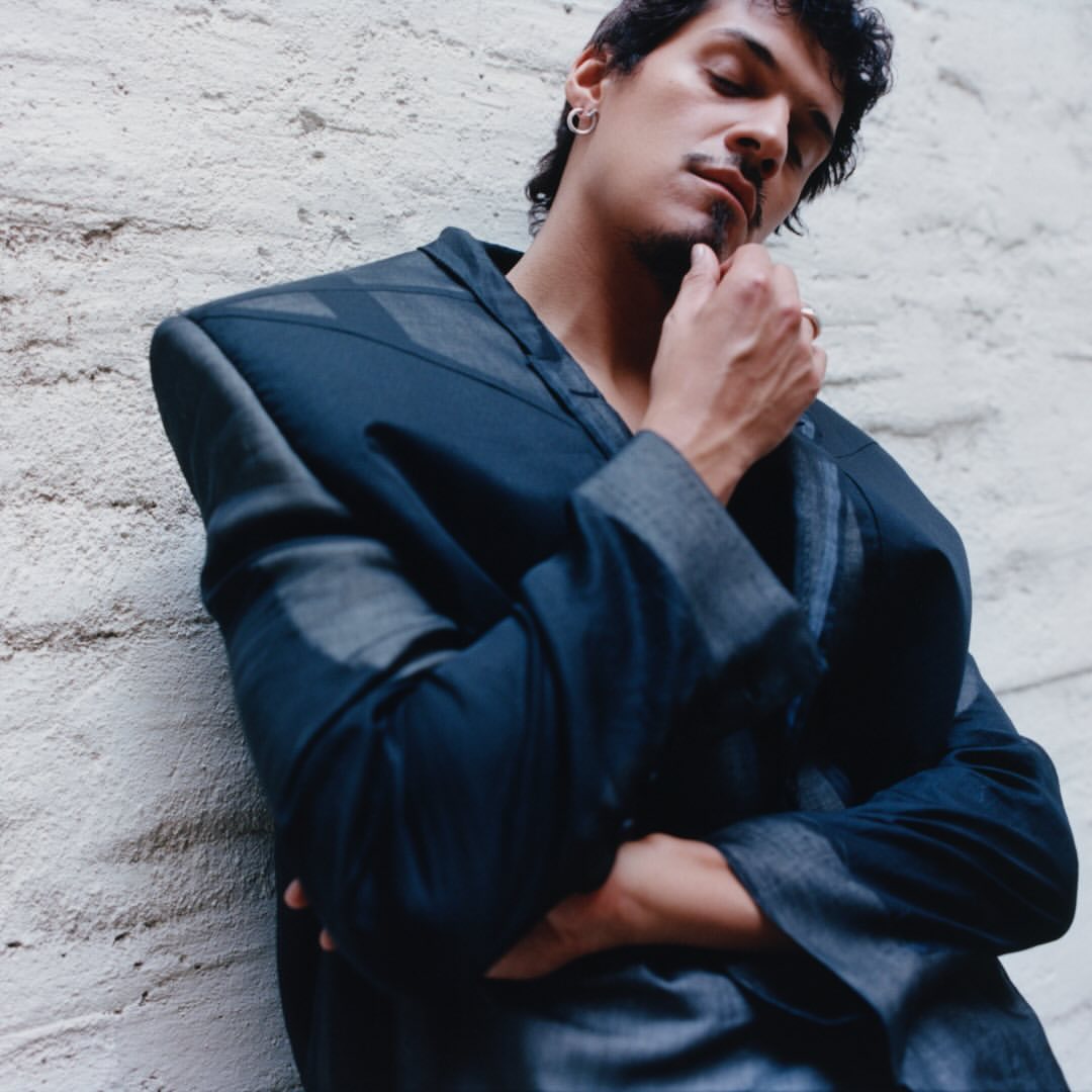 Adult male with a mustache in a dark blue textured jacket leaning against a white wall, close-up shot. Fashion photography.
