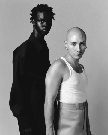 Black and white portrait of two models posing against a neutral backdrop, photographed by Ricky Alvarez.