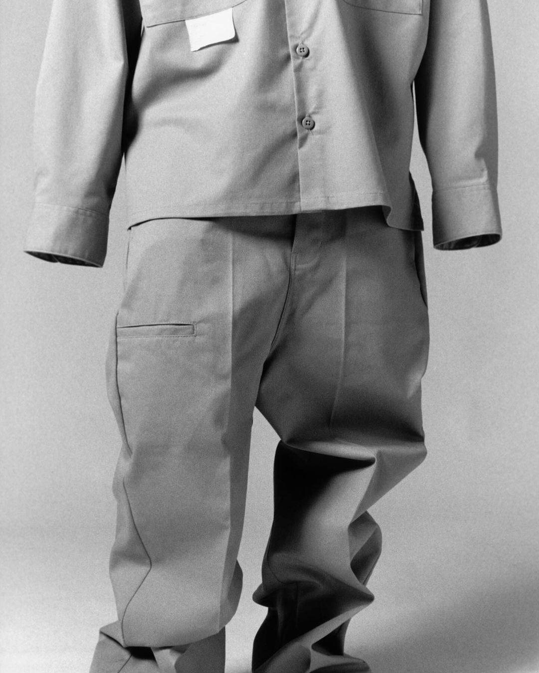 Studio shot of khaki-colored, long-sleeved collared shirt and pants ensemble on a gray background, featuring wrinkles and a blank tag.