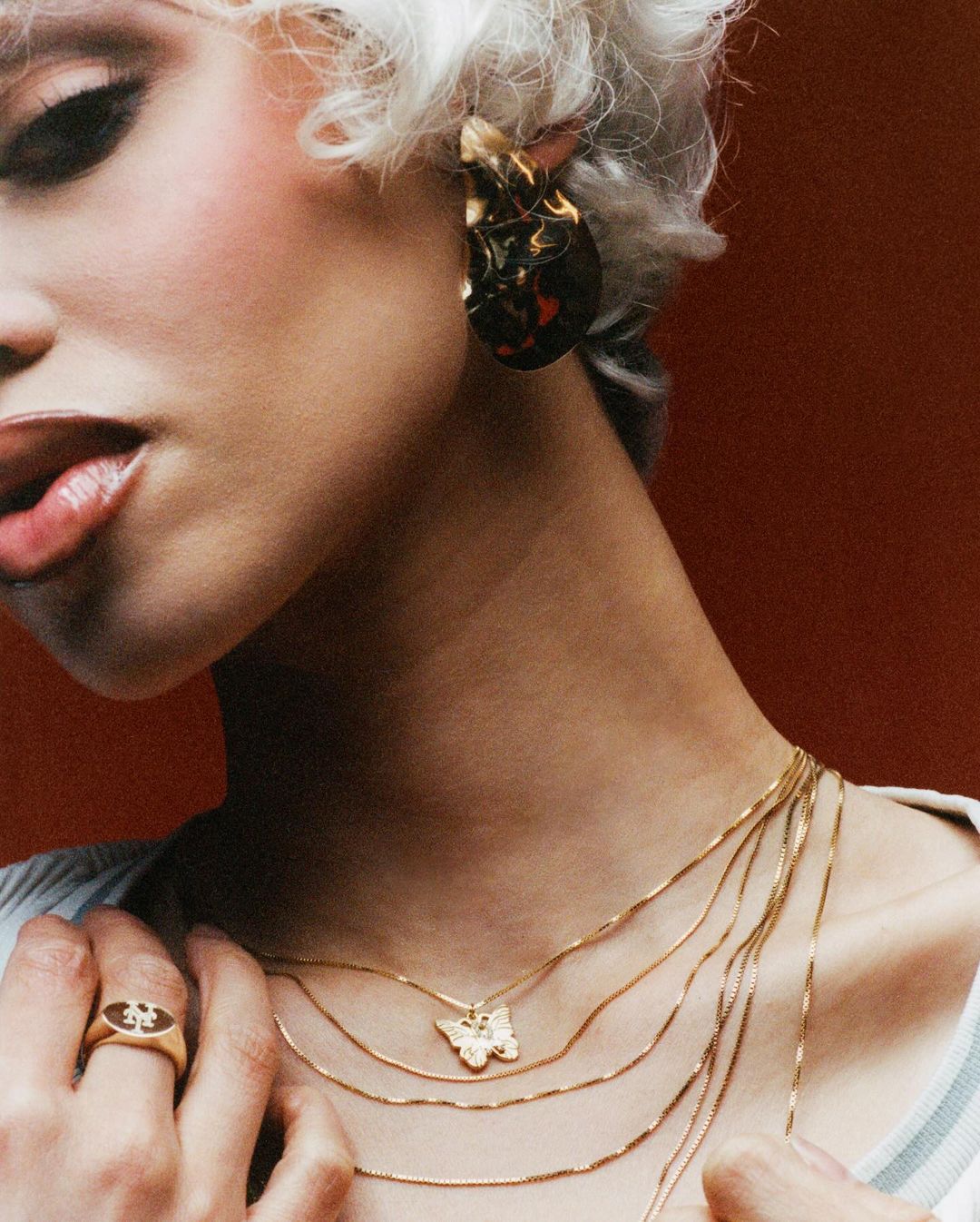 Close-up of a woman with platinum blonde hair wearing layered gold necklaces with a butterfly pendant and gold earrings.