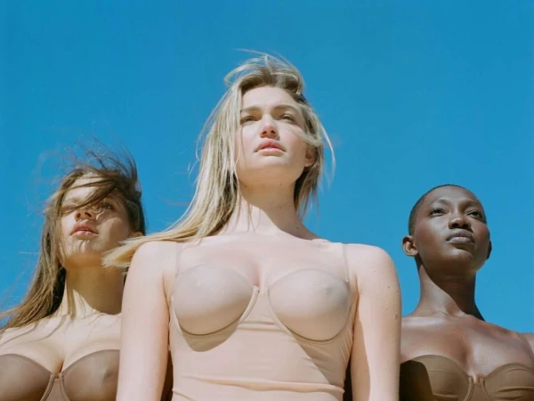 Three female models of diverse ethnicity wearing nude lingerie against a clear blue sky, fashion, beauty, portrait, eye-level shot.