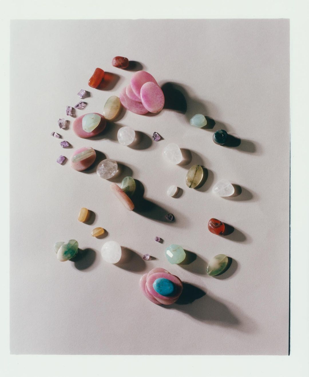 Overhead shot of assorted tumbled stones and polished gemstones in various colors, shapes, and sizes arranged on a neutral surface.